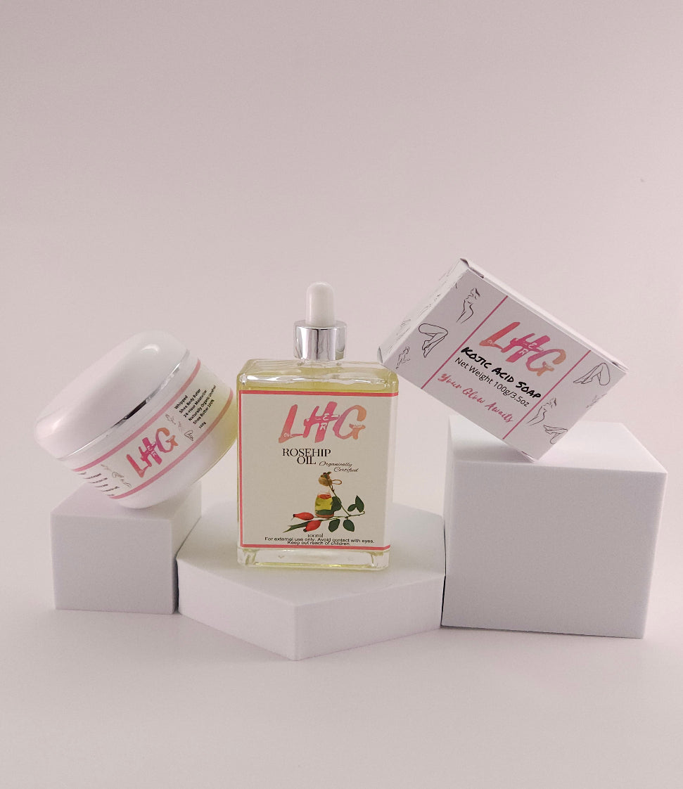 The image displays an assortment of skin care products from the LoveHerGlow brand, including a bottle of Rosehip Oil, a jar of Whipped Shea Body Butter, and a bar of Kojic Acid Soap, all presented against a neutral background.